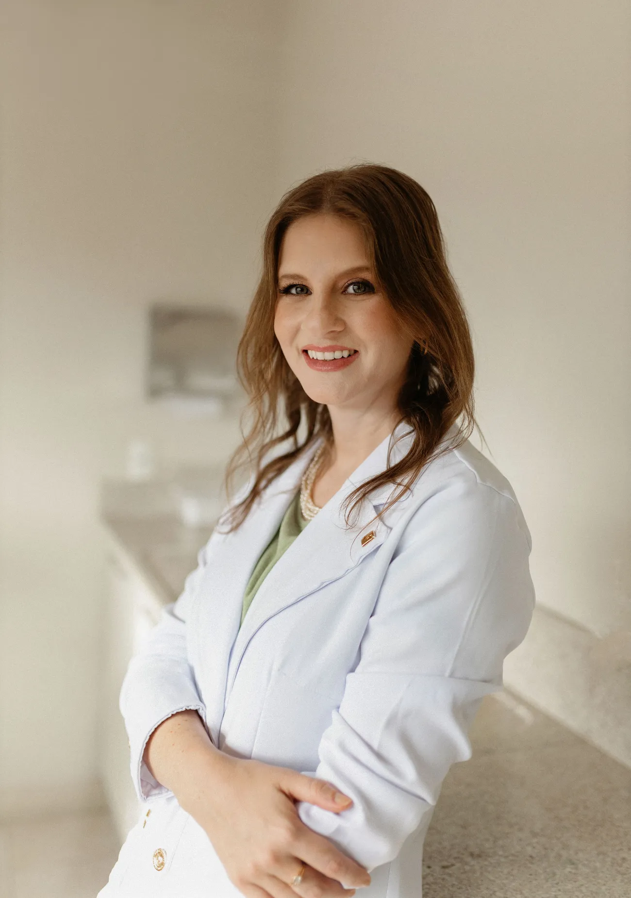 Dra. Laura Maccarini de jaleco branco, braços cruzados, sorrindo no consultório